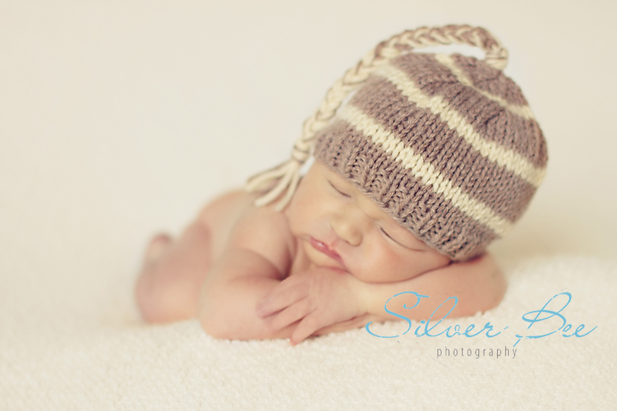 newborn boy sleeping on cream blanket with striped knitted hat