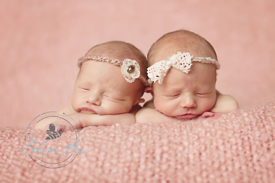 Identical twin baby girls sleeping on pink blanket with headbands by creme de la baby