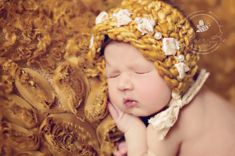 7 day old newborn girl posing on gold ruffled fabric with gold knitted and fabric bonnet, Austin Texas.