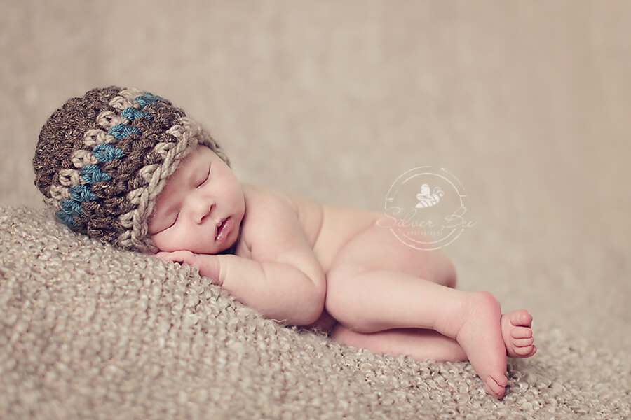 Austin newborn baby boy photo session sleeping on brown boucel blanket with striped earflap hat.