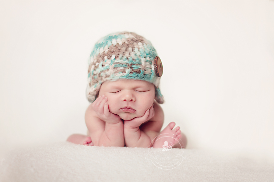 Newborn baby boy doing froggie pose with blue and brown earflap beanie hat in Austin Texas.