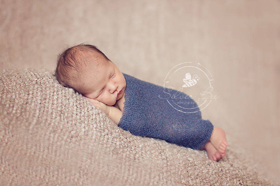 1 week old newborn baby boy posing on beige boucle blanket and blue denim stretch wrap in Austin Texas.
