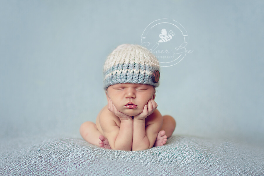 One week old baby boy in froggie pose with striped blue hat and blue texture blanket in Austin Texas newborn photography session.