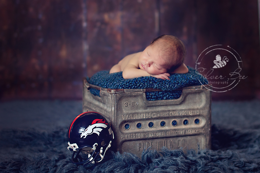 Austin TX baby boy sleeping in metal milk crate with blue boucle blanket and Denver Broncos baby helmet.