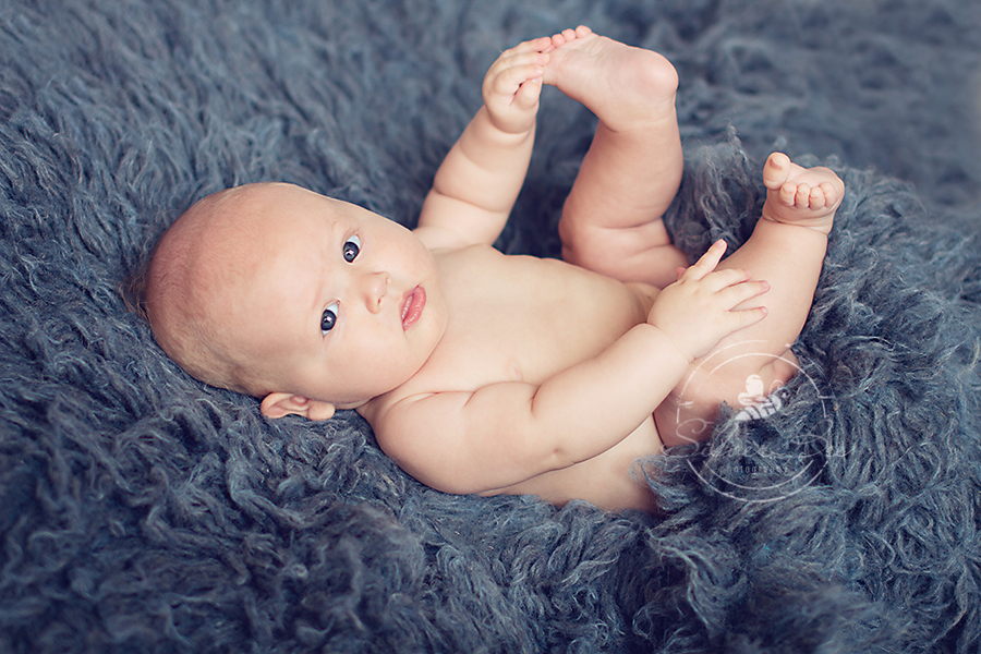 Austin baby three month old holding his feet for photography session on blue flokati rug.
