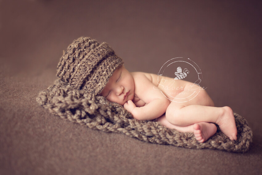 Austin Texas newborn baby is sleeping for his photography session with a brown brim hat and blanket.