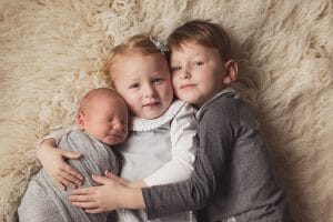 Big brother and sister holding newborn baby for photos