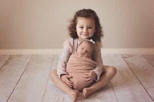 Big sister holding newborn sister in peach tones