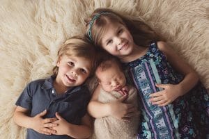 Big sister and big brother taking photo with newborn brother