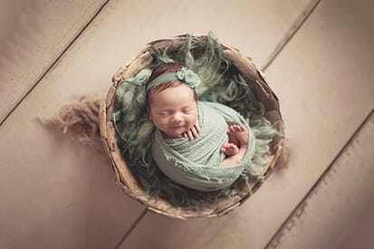 newborn wrapped in sage and posed in bowl